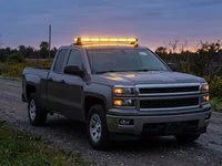 An amber light bar on the roof of a pickup truck at dusk on a quiet country road