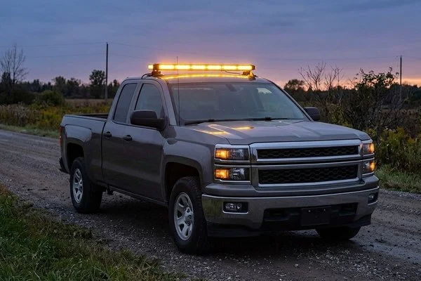 An amber light bar on the roof of a pickup truck at dusk on a quiet country road