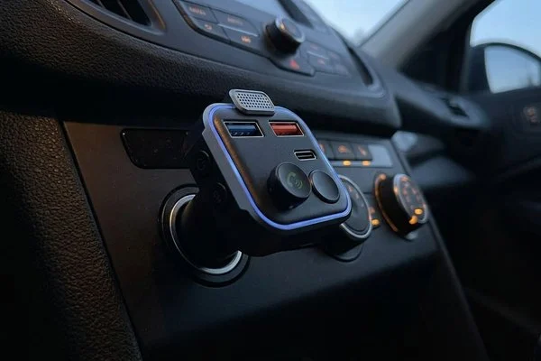 A small plug-in adapter with a soft blue ring light in a car dashboard power socket at dusk